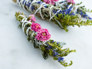 dried sage smudge sticks with pink flowers against marble background