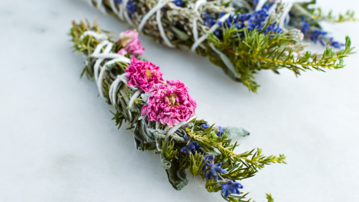 dried sage smudge sticks with pink flowers against marble background