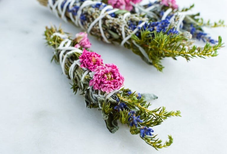 dried sage smudge sticks with pink flowers against marble background