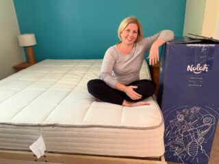 woman sitting on natural mattress with blue shipping box nearby