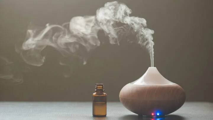 essential oil diffuser with nearby brown glass bottle against a dark background