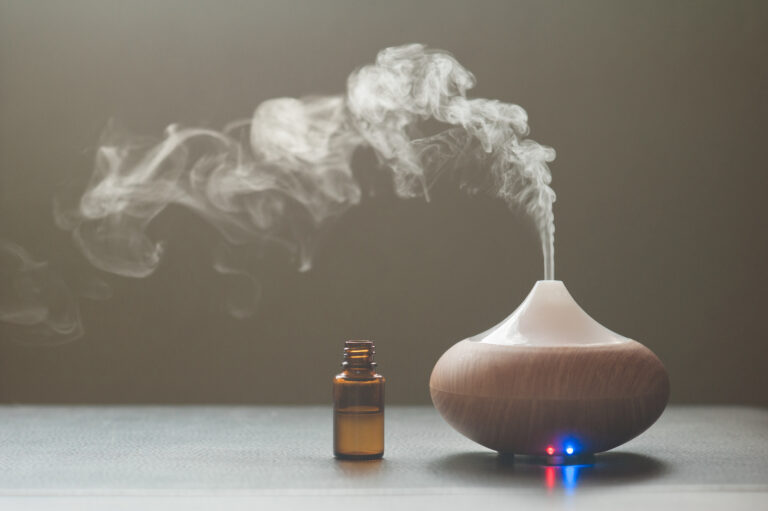 essential oil diffuser with nearby brown glass bottle against a dark background