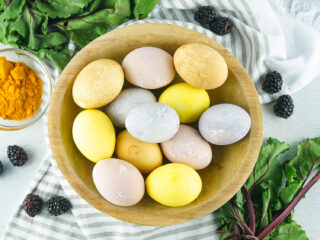 naturally colored Easter eggs in a wooden bowl with plants and spices around it