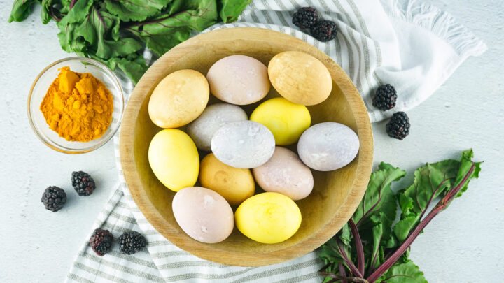 naturally colored Easter eggs in a wooden bowl with plants and spices around it