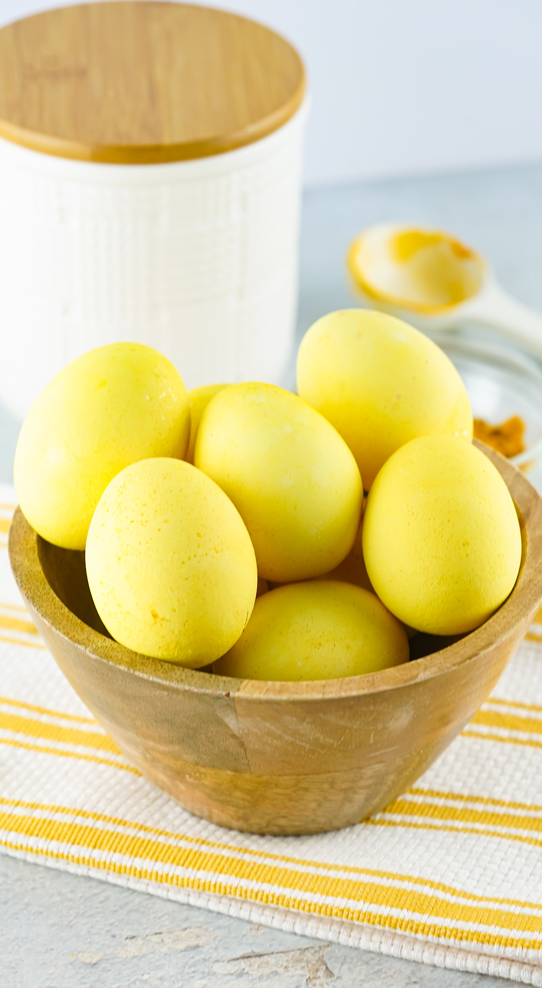 Yellow colored eggs in wooden bowl with white canister in background