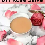 small aluminum tin filled with pink colored rose salve on marble background with fresh rose laying beside it