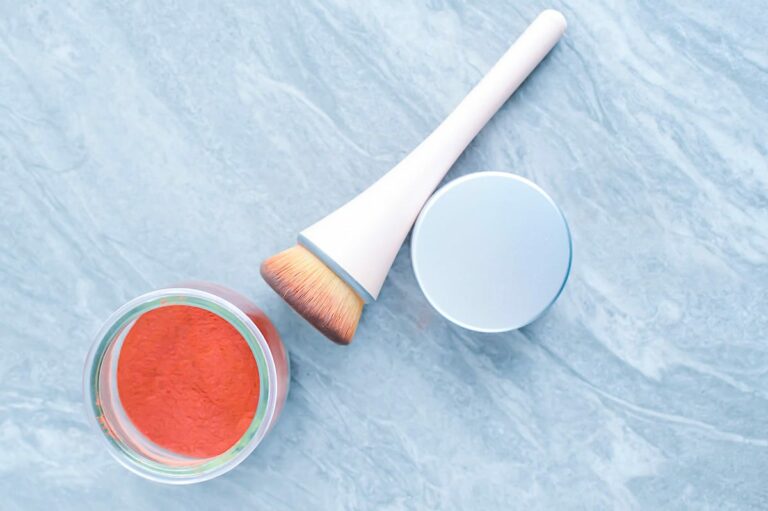 A jar of orange powder, a makeup brush, and a closed lid.