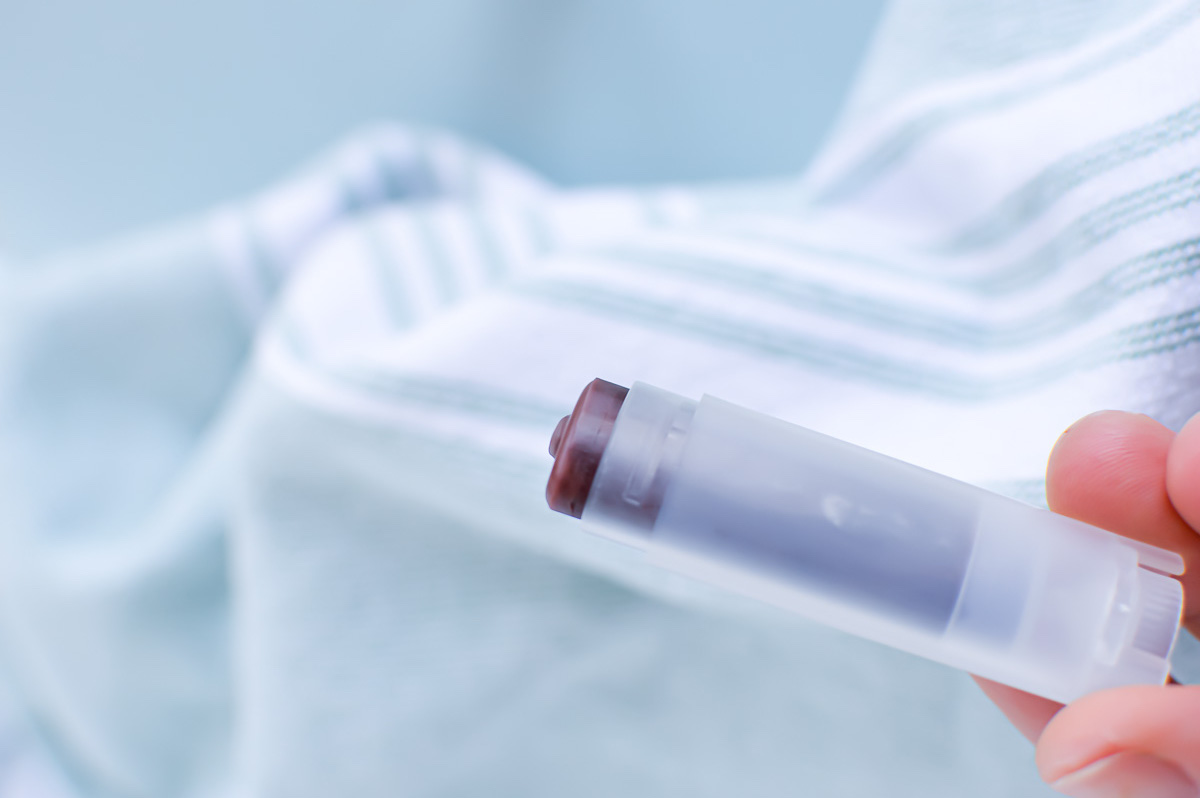 Beetroot Lip Balm in clear tube being held in persons hand against light blue background