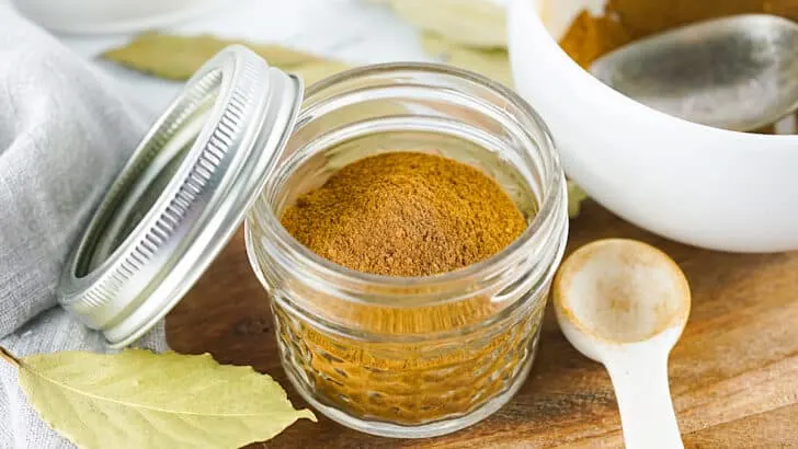Pumpkin Pie Spice in a clear glass jar with a metal lid sitting on a wood cutting board