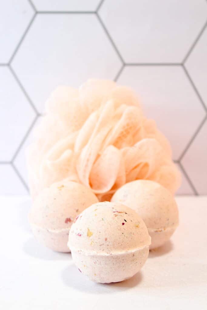 Rose Petal Bath Bomb cluster with shower luffa against light colored tiles