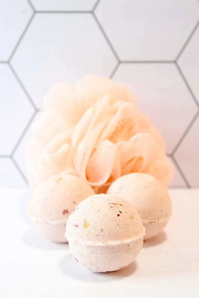 Rose Petal Bath Bomb cluster with shower luffa against light colored tiles