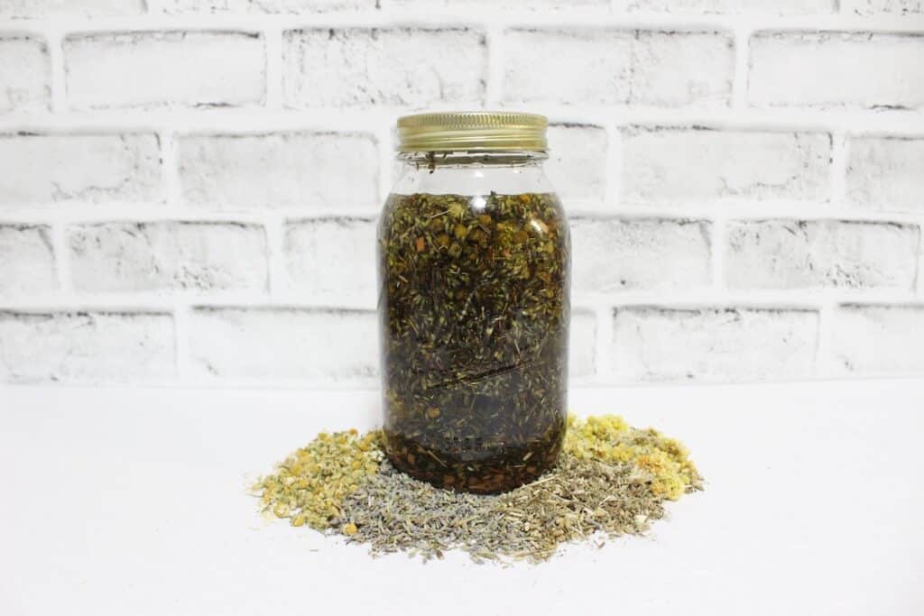 Cramp Cream Step 1 with a jar with dried herbs on top of a brick wall.