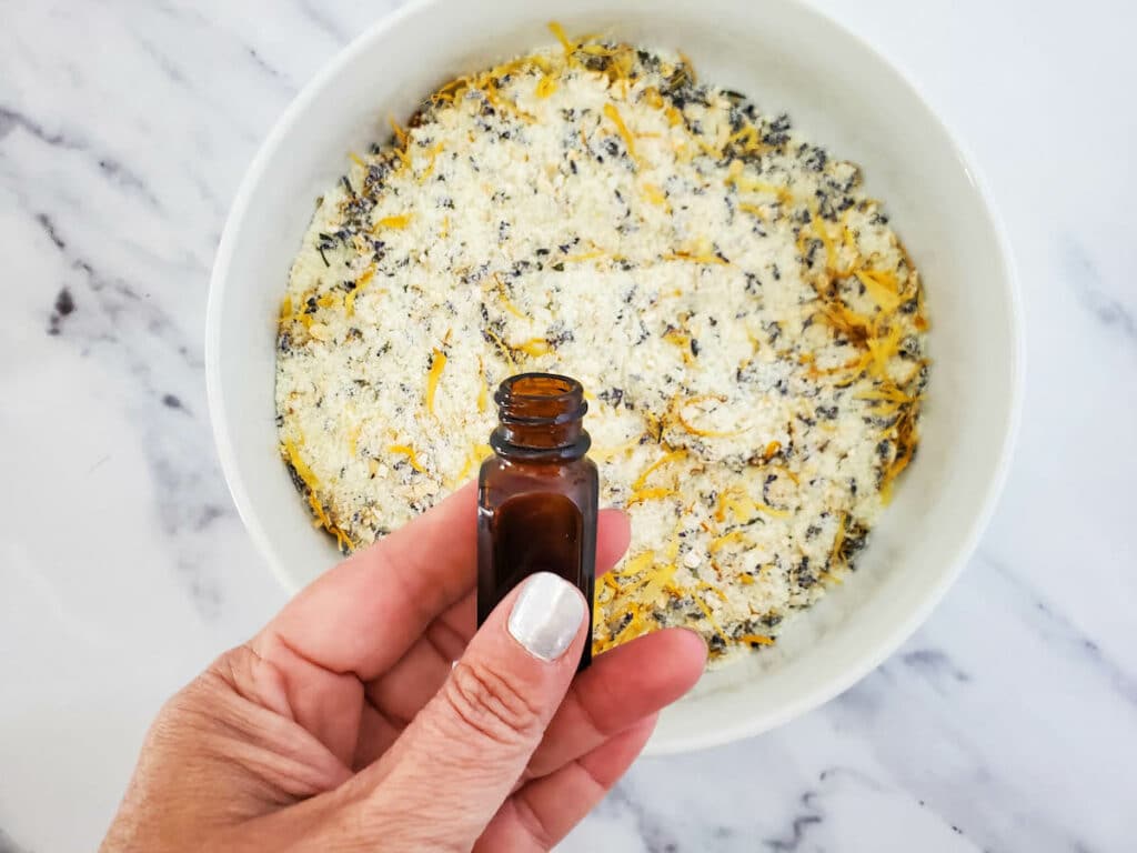 A person holding a bottle of essential oil in a bowl.