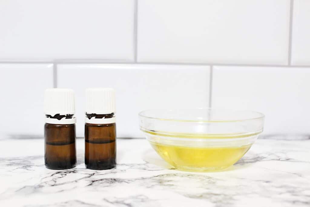 Two bottles of essential oils and a bowl of oil on a marble counter to make DIY Vanilla Perfume.