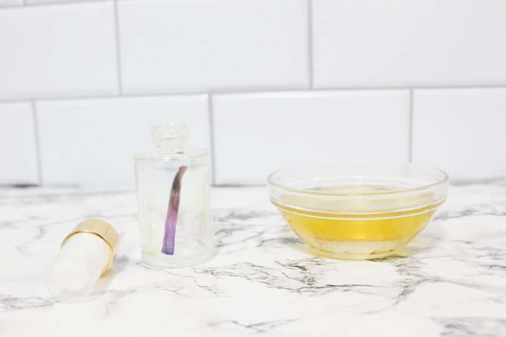 A bottle of essential oil and a glass of water on a marble counter to make DIY Vanilla Perfume.