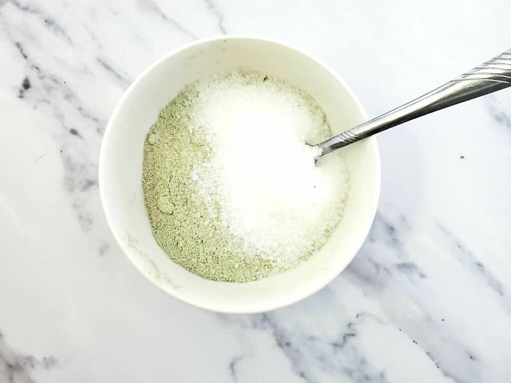 A bowl of green powder with a spoon in it.