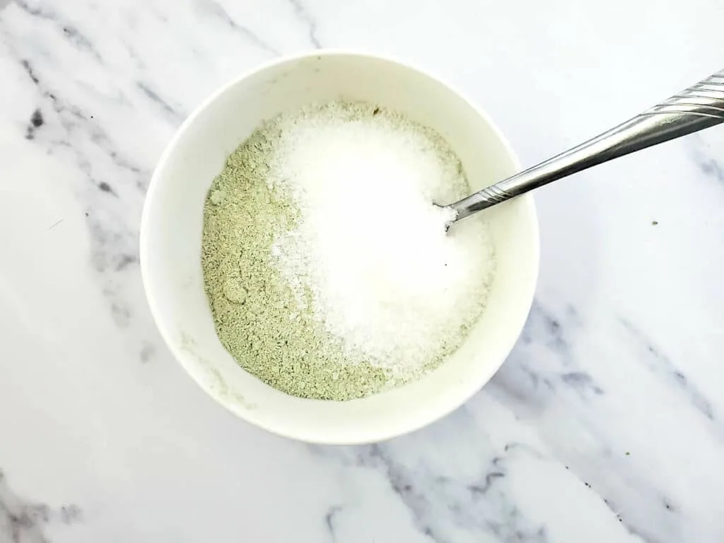 A bowl of green powder with a spoon in it.