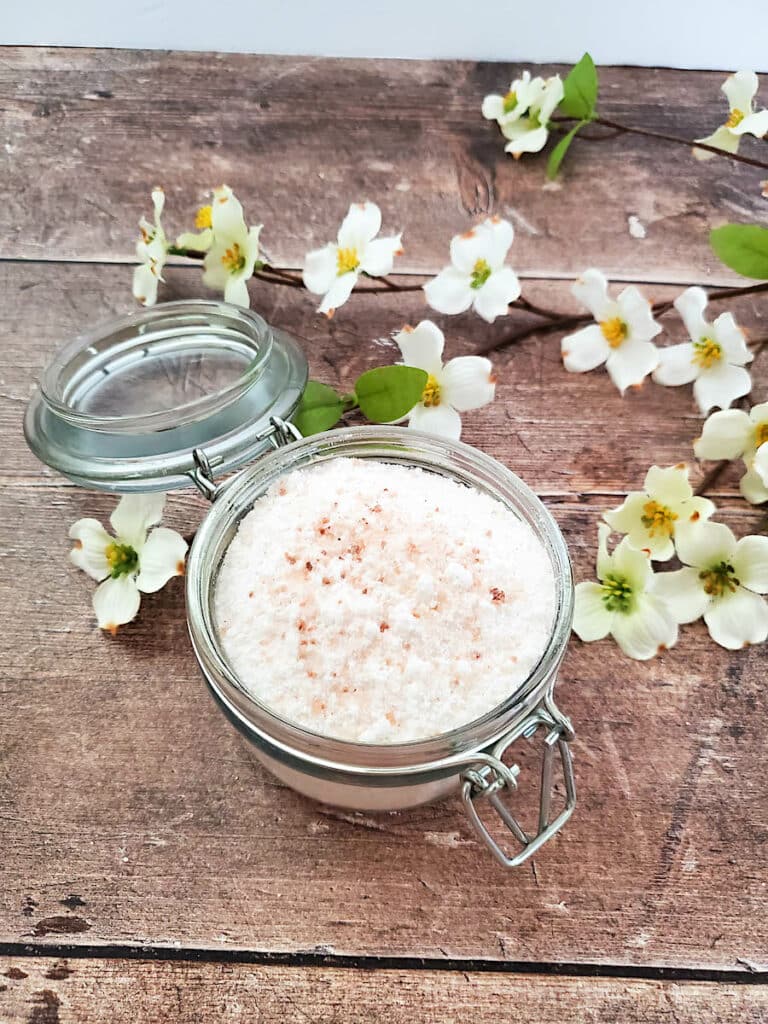 A jar of fizzy bath salts on a wooden table with white flowers.