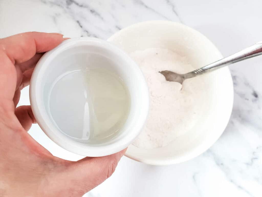 A person holding a bowl of water and a spoon to make fizzy bath salts.