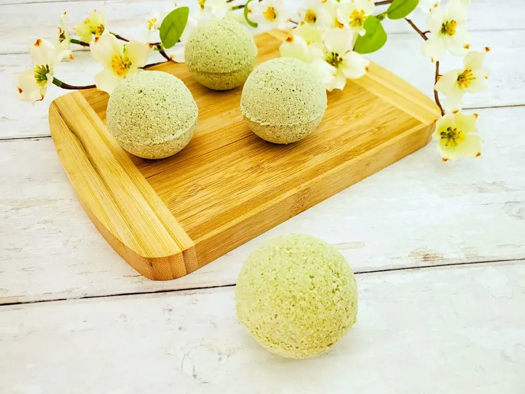 Three green lemongrass bath bombs on a wooden cutting board.