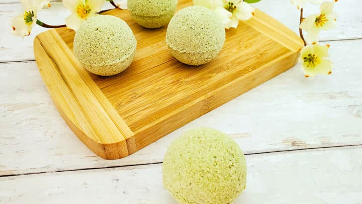 Three green lemongrass bath bombs on a wooden cutting board.