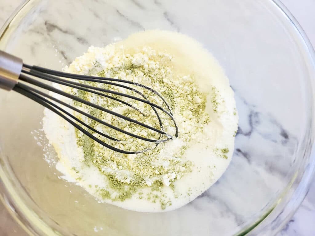 A whisk with lemongrass bath bombs mixture in a glass bowl.