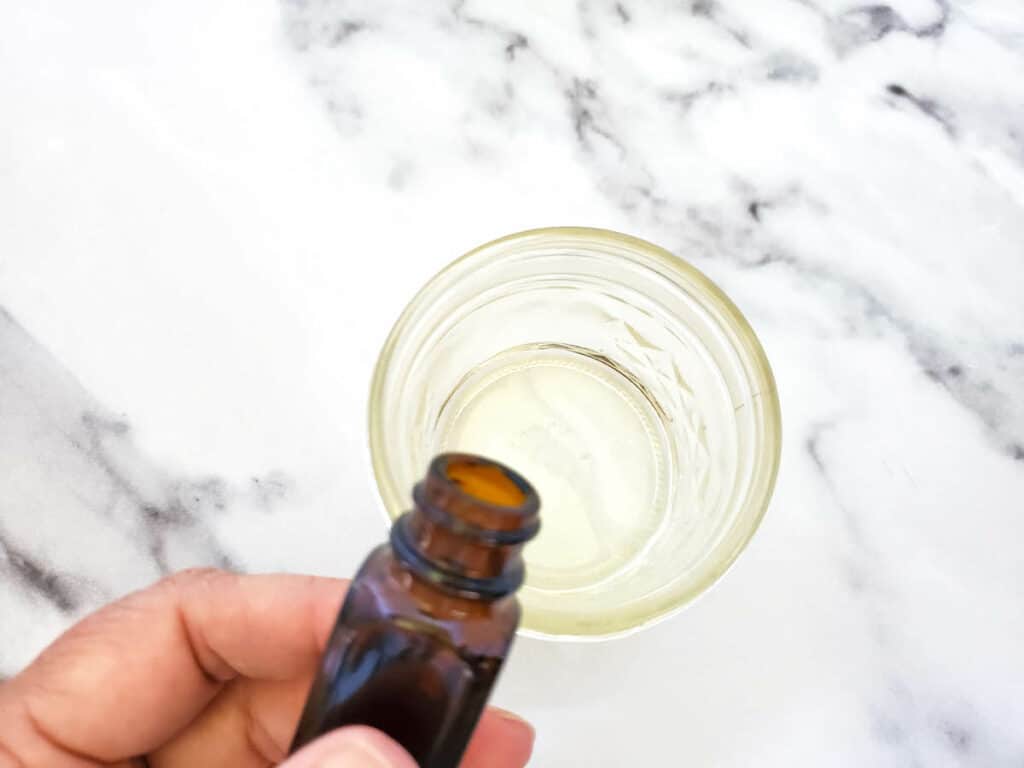 A person holding an essential oil bottle on a marble countertop.