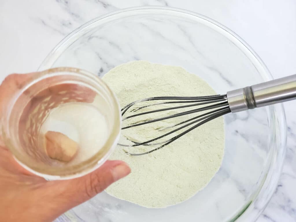A person is whisking lemongrass bath bombs mixture in a glass bowl.