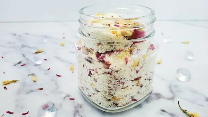 A jar of milk and honey floral bath soak ingredients in a glass jar on a white marble table.