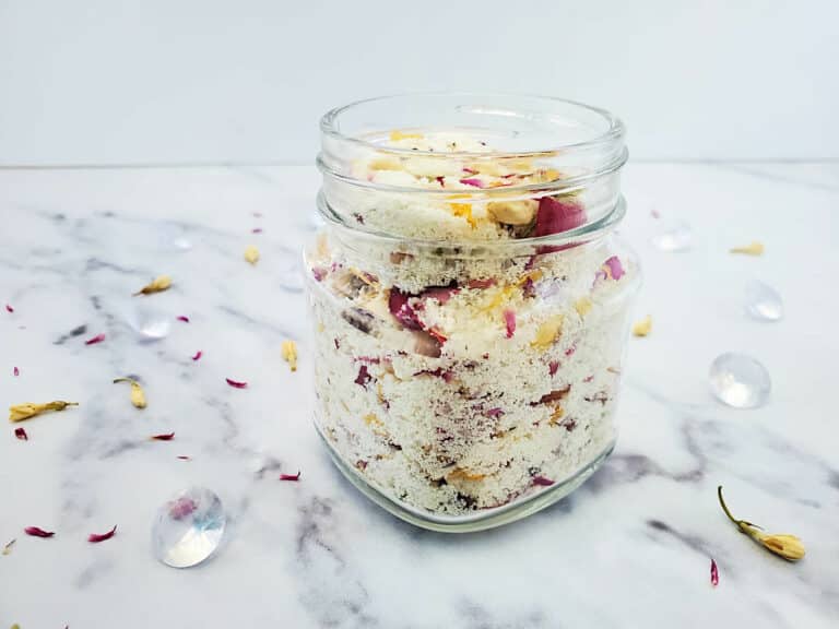 A jar of milk and honey floral bath soak ingredients in a glass jar on a white marble table.