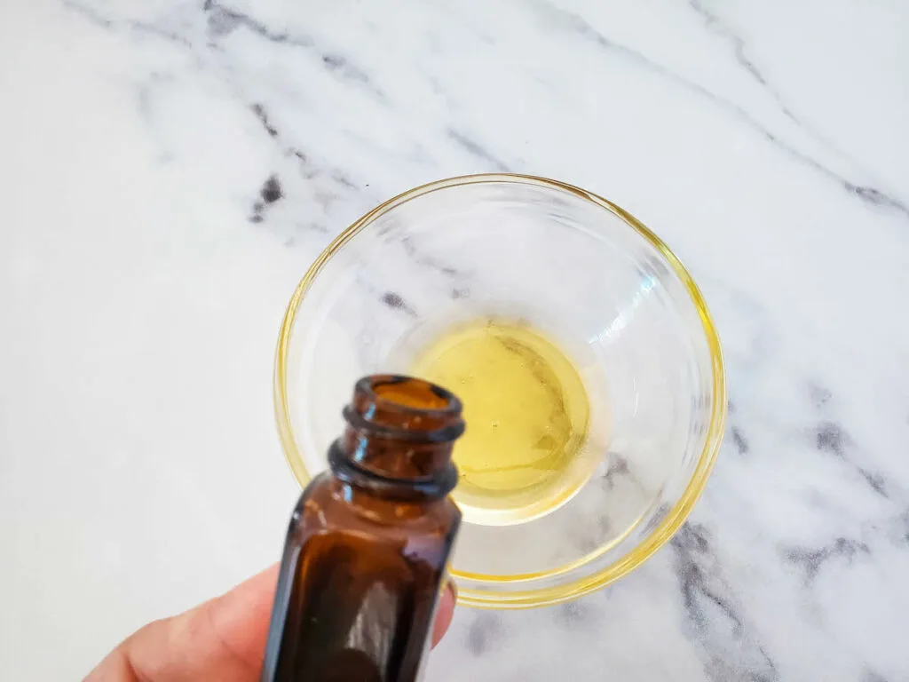 Essential oils poured into a glass bowl for a milk and honey floral bath soak recipe.