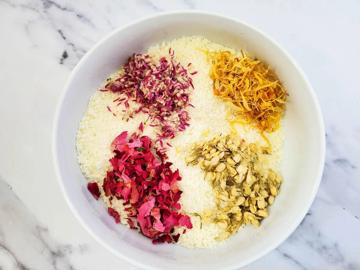 A white bowl with various milk and honey floral bath soak ingredients in it.