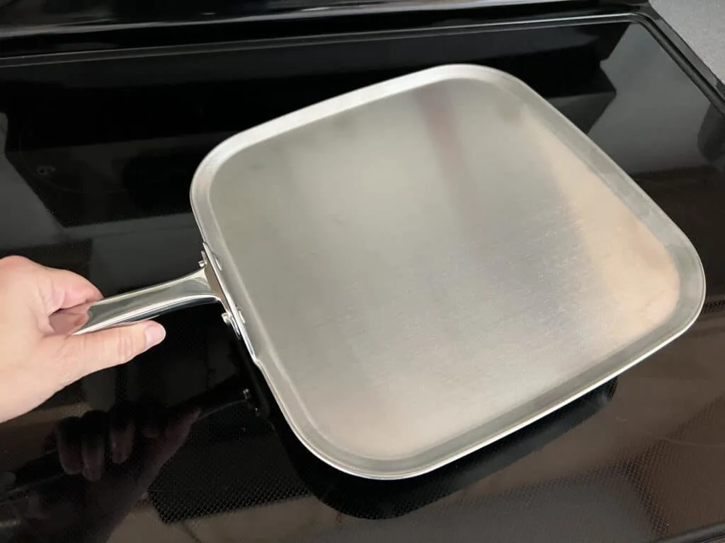 A person holding a stainless steel pan on top of a stove, using 360 cookware.