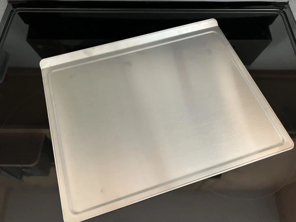 A 360 cookware stainless steel baking sheet sitting on top of a stove.