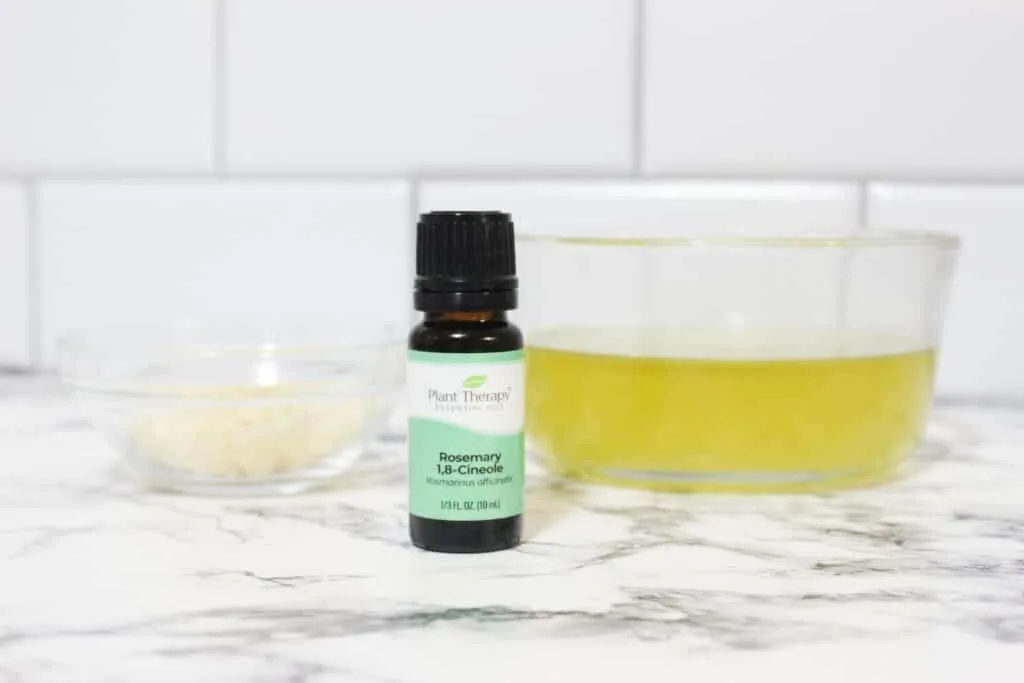 A bottle of rosemary essential oil next to a bowl of ingredients.