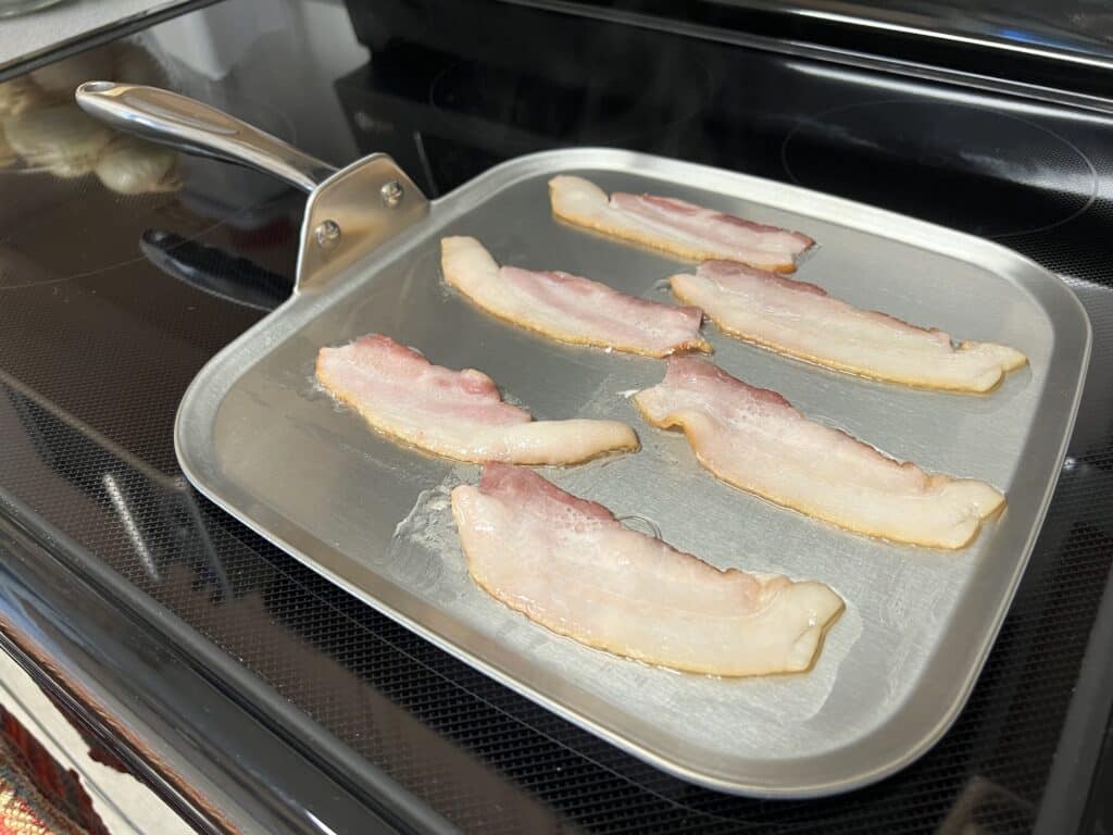 A 360 cookware pan with bacon sizzling on it.
