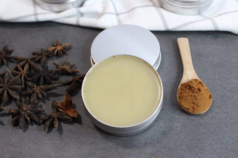 Star anise salve in a tin with a wooden spoon and whole spices nearby.