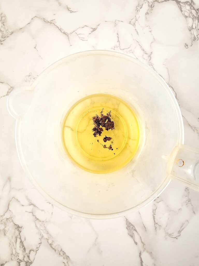 Vanilla Homemade Lotion Bar Step 4 - A glass bowl filled with a mixture of oil and flowers.