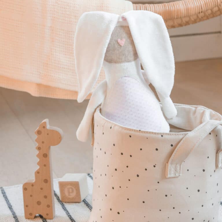 A plush bunny toy sitting in a minimalist Easter basket alongside a wooden giraffe toy and a wooden block.